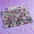 Rectangular wristlet clutch featuring a dark background with colorful bats, skulls, eyeballs, and vampire mouths. White strap and gold zipper visible.